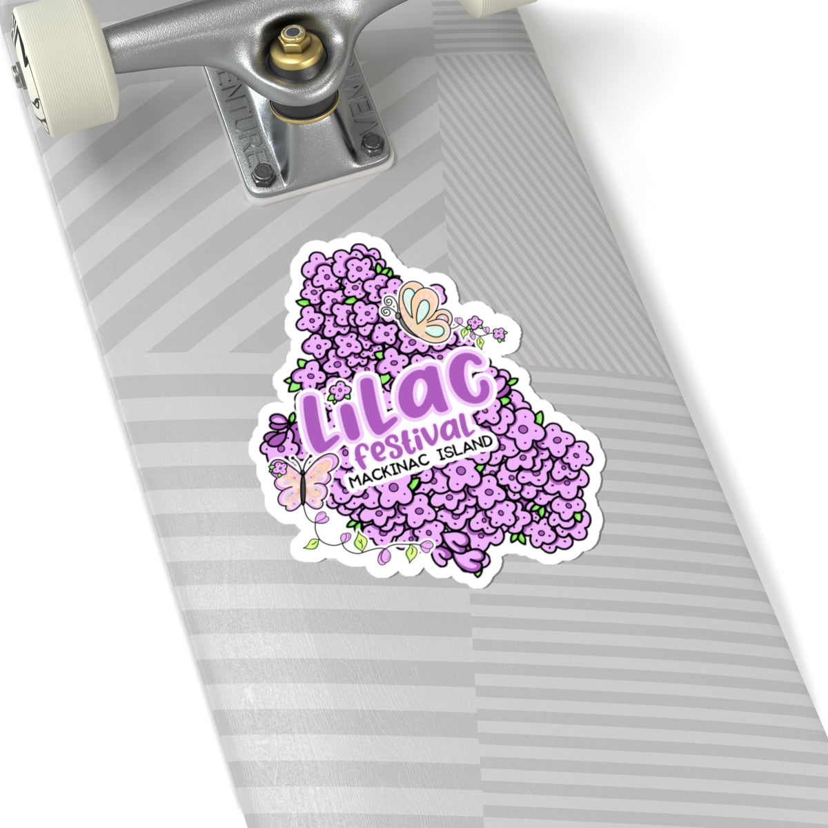 A die-cut sticker featuring the text 'Lilac Festival' and 'Nassauic Island' surrounded by purple flowers and butterflies, shown applied to the underside of a skateboard deck.