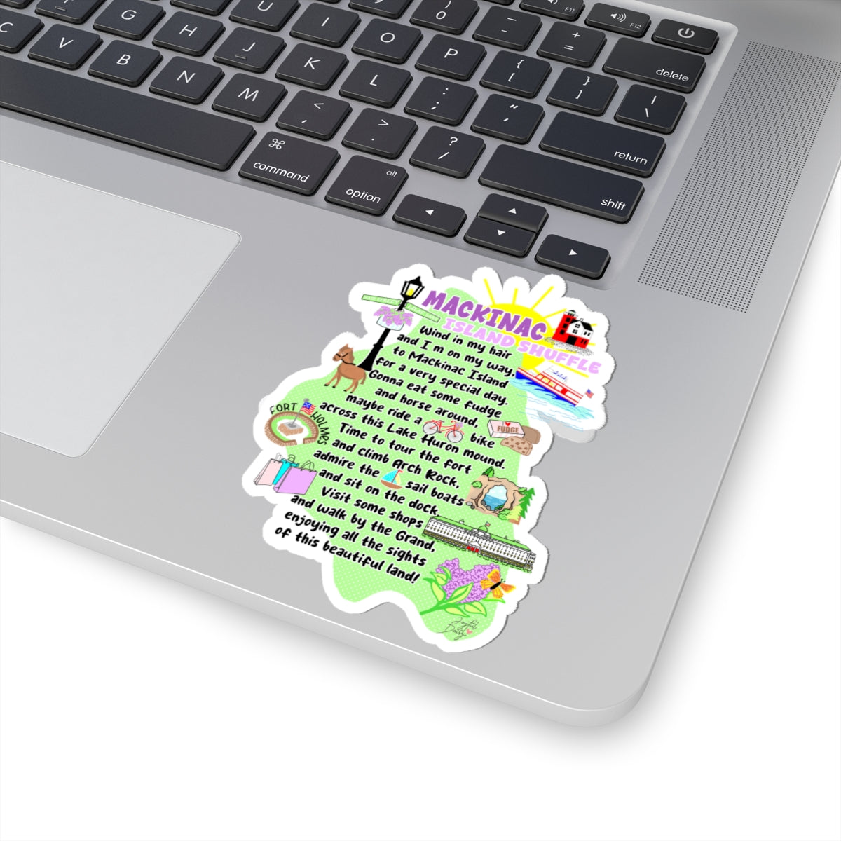 A colorful die-cut sticker shaped like a tree, featuring the text 'MACKINAC WILDFLOWERS' and a whimsical illustrated poem, shown applied to the lower corner of a silver laptop keyboard.
