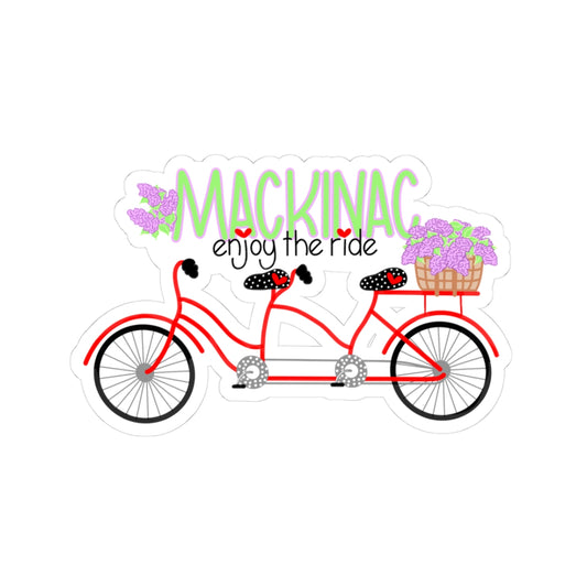 A die-cut sticker featuring a red tandem bicycle with black seats, purple flowers in the rear basket, and the text 'MACKINAC enjoy the ride' in green and black lettering, shown on a plain white background.
