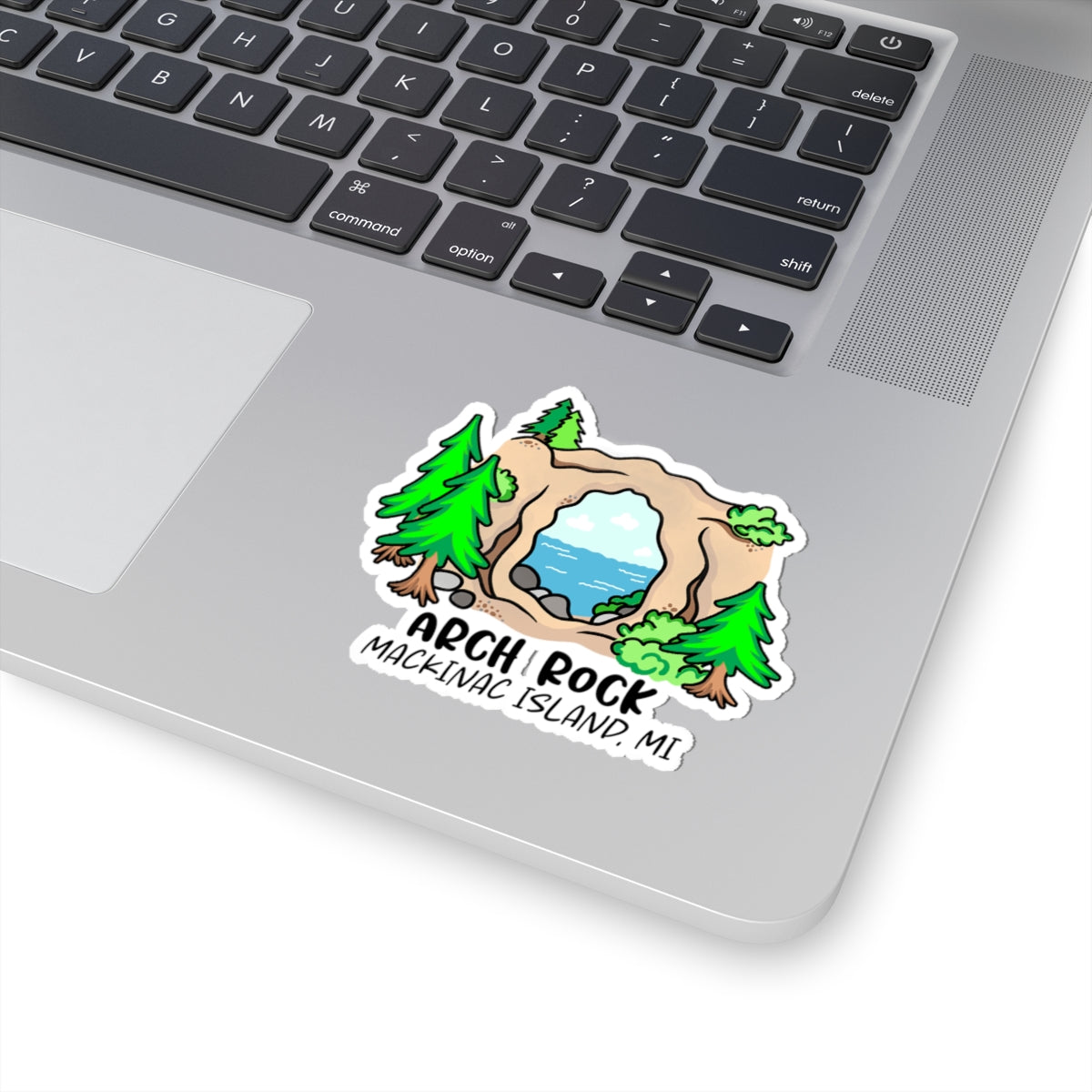 A die-cut vinyl sticker of Arch Rock on Machigag Island, Michigan, shown applied to the silver palm rest of a laptop keyboard.