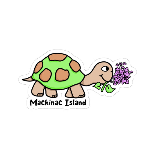 A die-cut sticker featuring a cartoon turtle with a green shell and brown spots, eating purple flowers, with the text 'Mackinac Island' below on a white background.