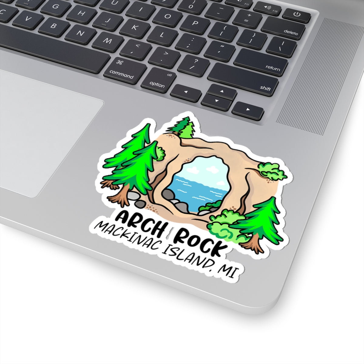 A die-cut vinyl sticker of Arch Rock on Mackinac Island, MI, shown applied to the silver surface of a laptop keyboard.