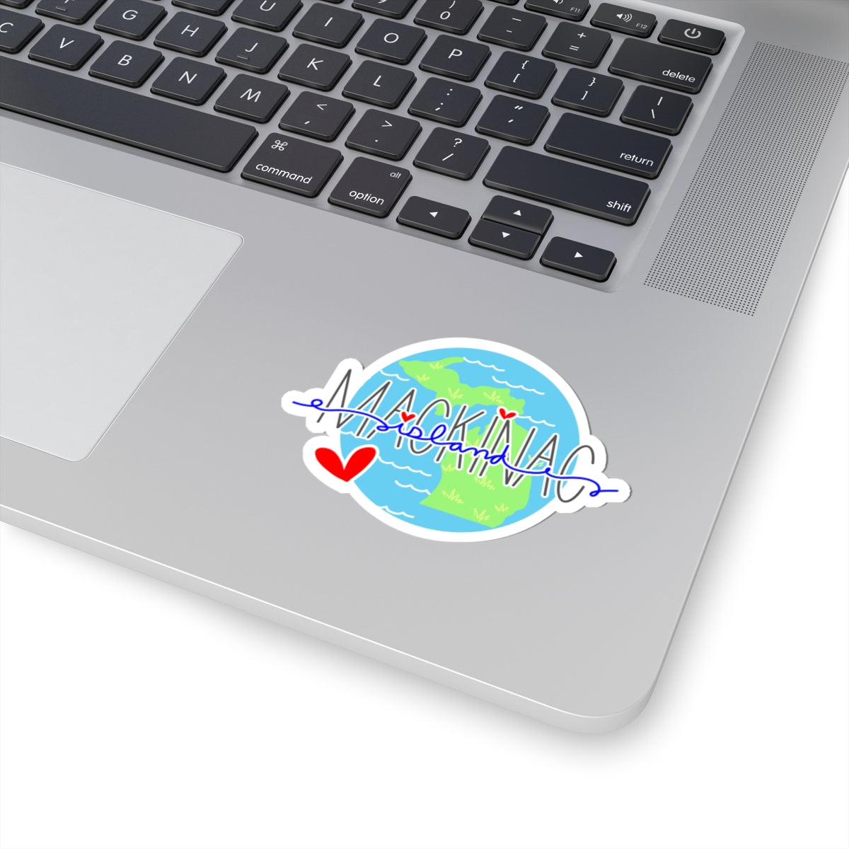 A die-cut vinyl sticker applied to the silver trackpad area of a laptop. The sticker features a colorful globe graphic with blue oceans and green land, overlaid with a white cursive script reading 'MCKINNEY' and small red hearts.