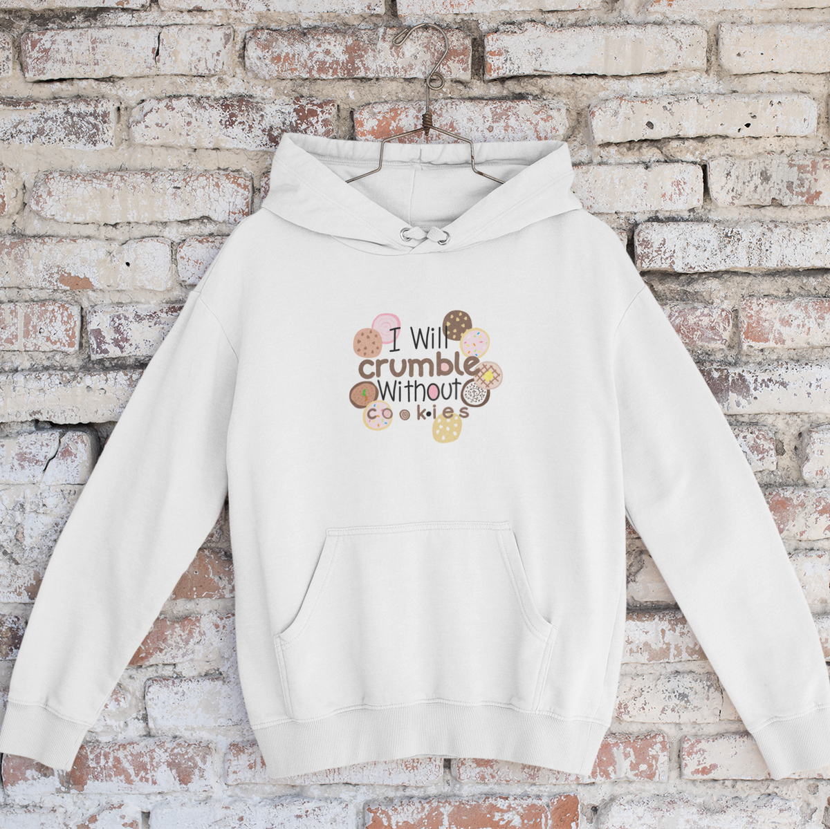 most popular teenage girl gift in pink and white pullover hoodie with a graphic print that reads 'I will crumble without cookies' surrounded by various cookie illustrations, hanging against a rustic white and red brick wall.