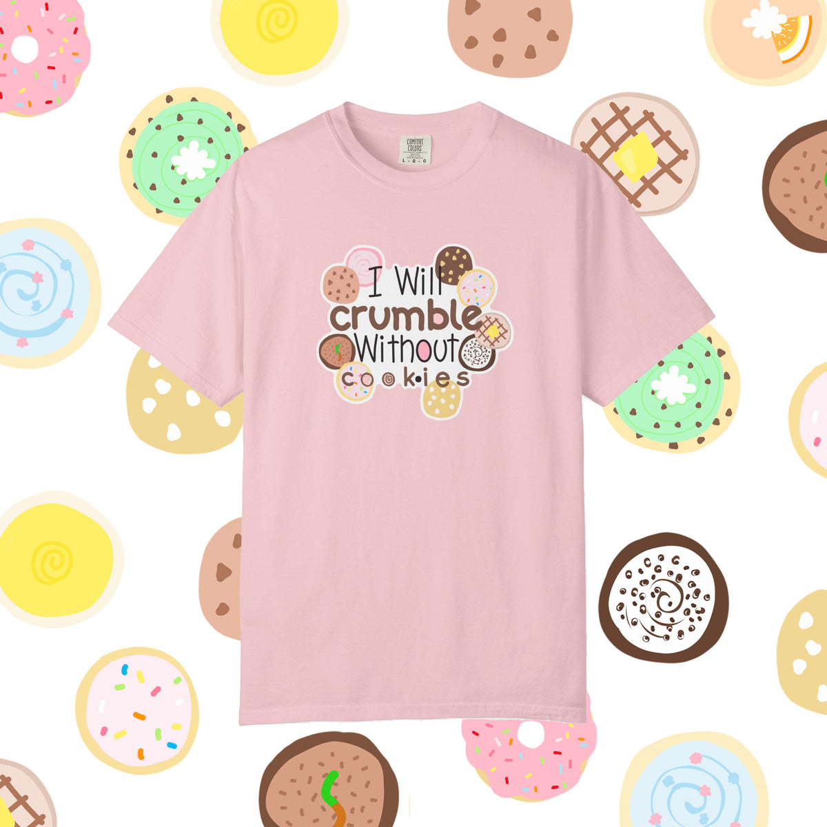 A light pink short-sleeve t-shirt with a graphic that reads 'I Will crumble without cookies' surrounded by various illustrated donuts, set against a white background patterned with donuts.