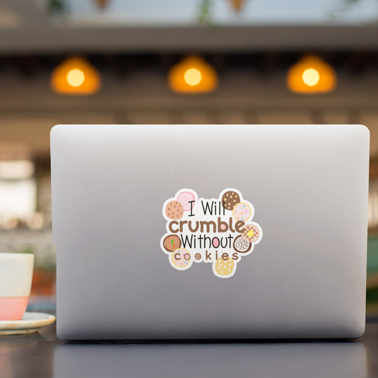 A silver laptop on a table in a cafe setting, featuring a die-cut sticker on the back with the text 'I Will crumble Without cookies' surrounded by illustrated cookies.