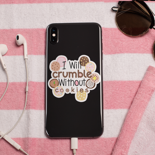 A black phone case with a cute cookie graphic and the text 'I Will crumble Without cookies' is displayed on a pink and white striped blanket. The scene is styled with white earbuds, sunglasses, and a charging cable.