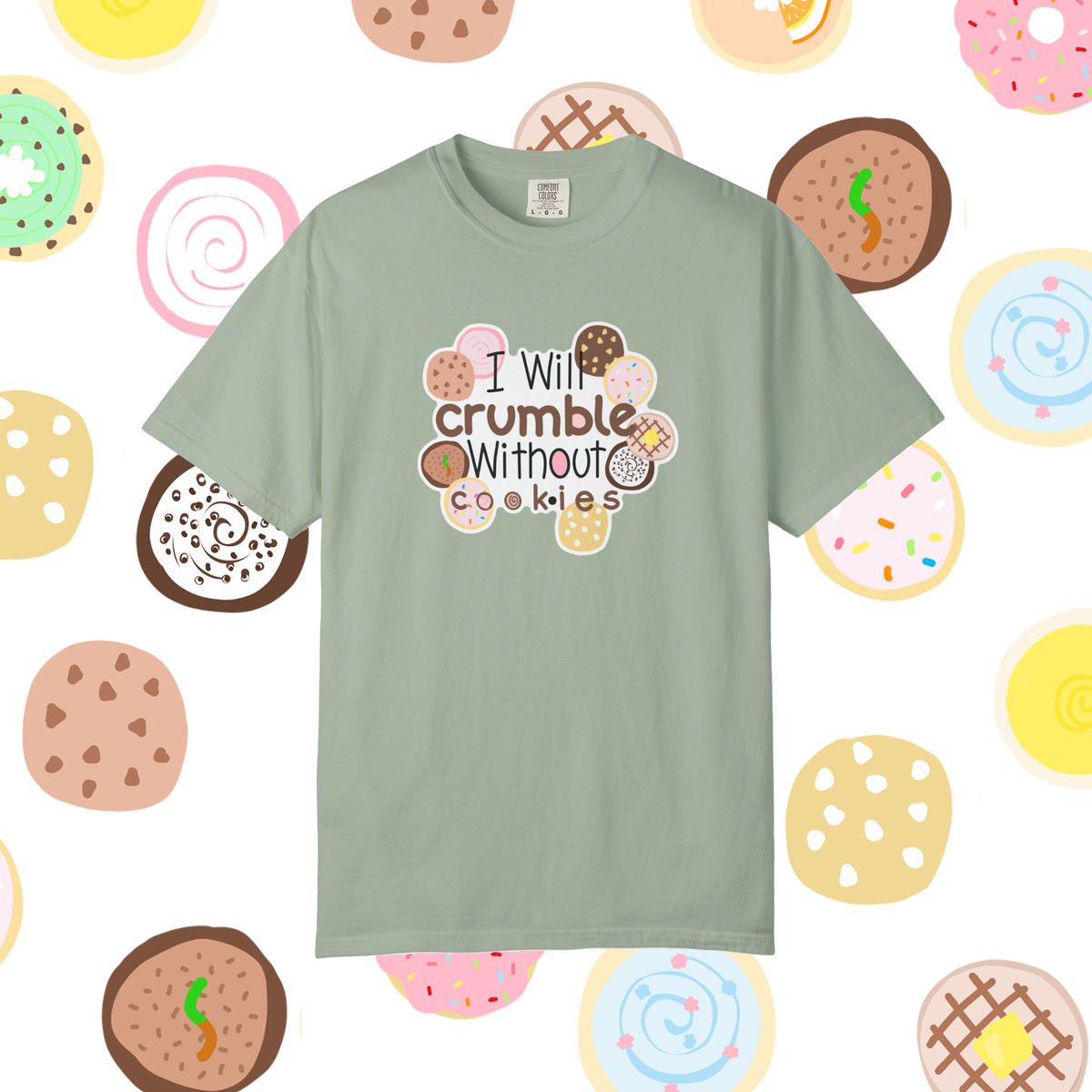 A sage green short-sleeve t-shirt with a graphic that reads 'I Will crumble Without cookies' surrounded by illustrated donuts, set against a white background patterned with colorful donuts.